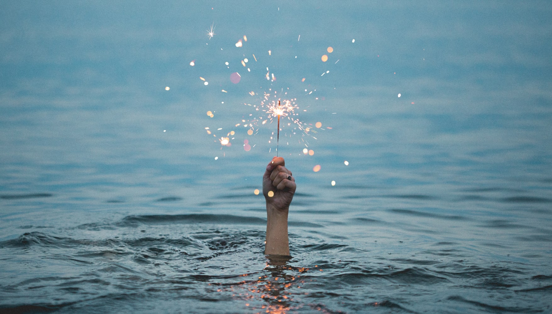 A person drowing in a lake holding sparklers as they drown