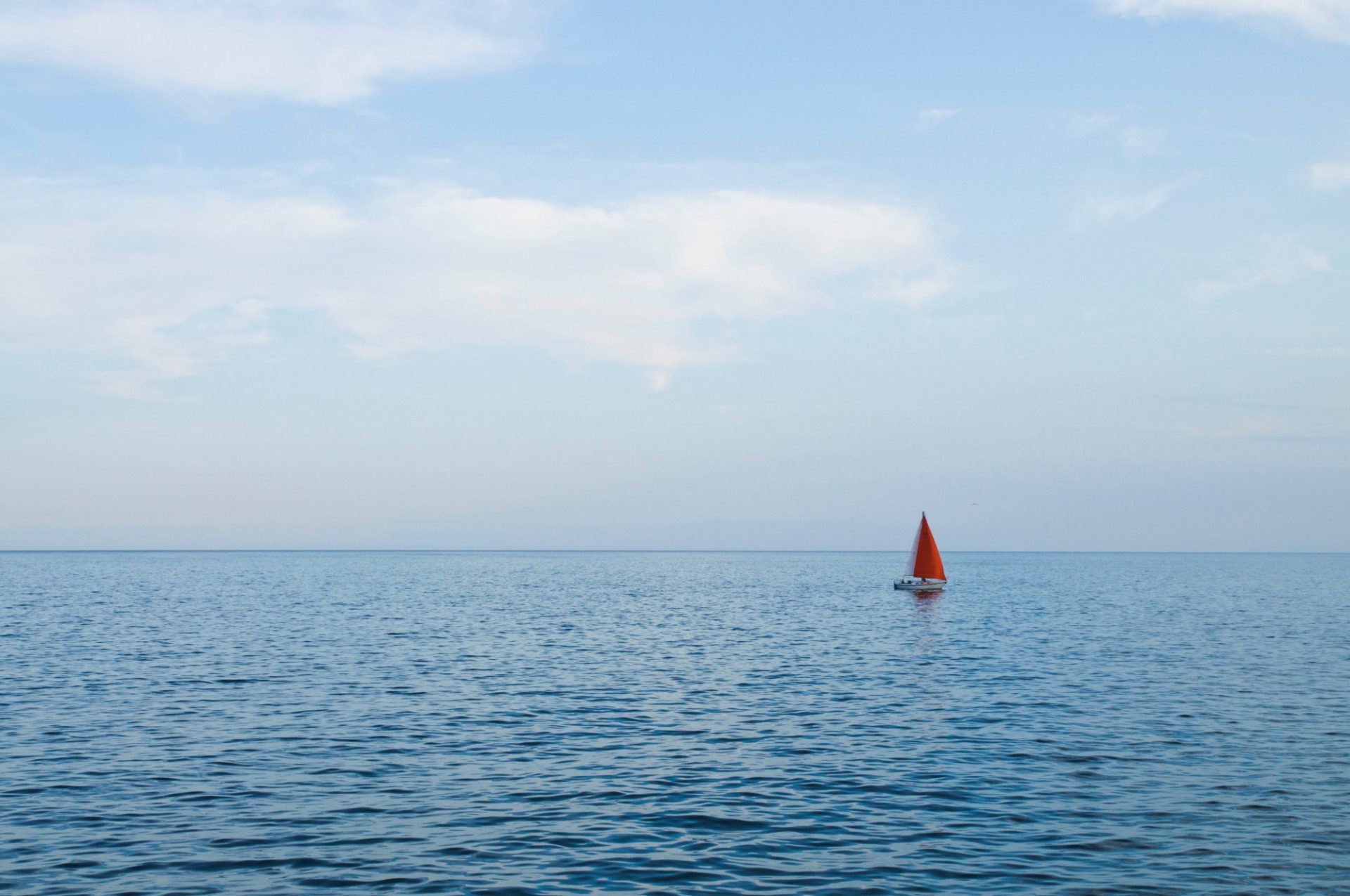 A lone red boat swimming in a vast blue ocean
